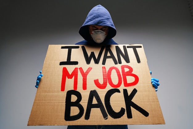 Foto bordje 'ik wil mijn baan terug' in handen van demonstrant met masker