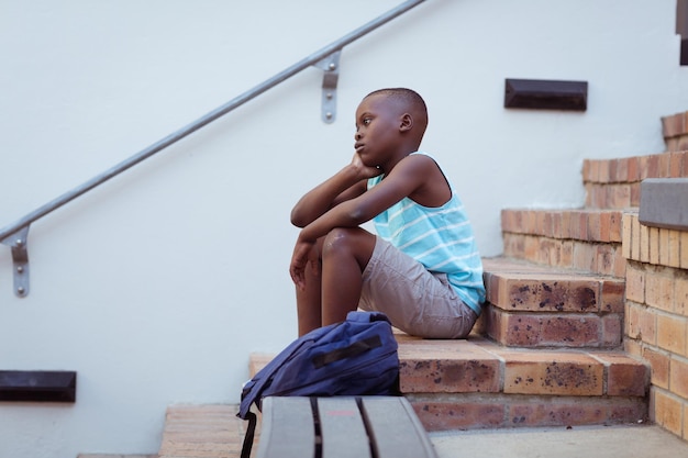 Bored african american schoolboy sitting on steps in school yard