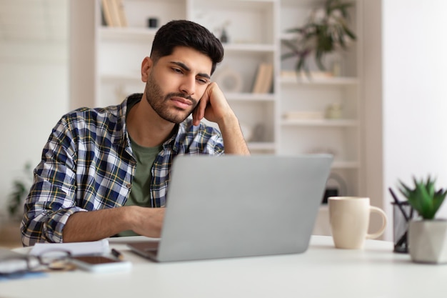 Bored arab male worker sitting at desk with pc