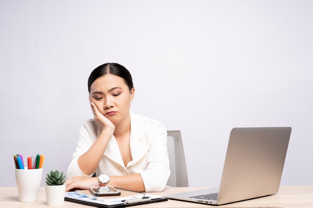 Bored businesswoman using laptop while sitting at desk against white background