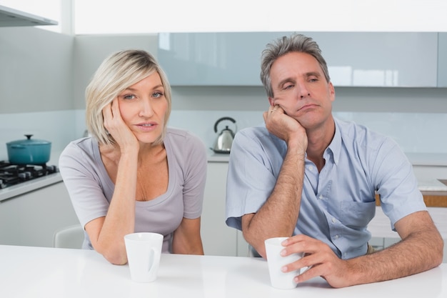 Foto coppie annoiate che si siedono con le tazze di caffè in cucina