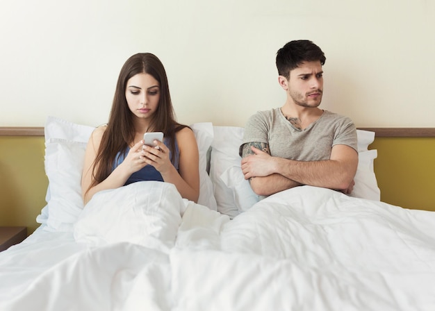 Bored couple and worried man by his wife smartphone addiction