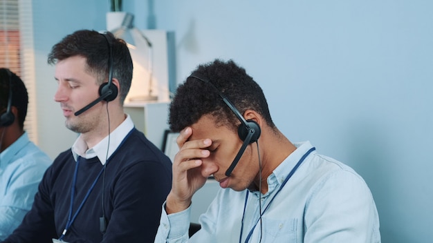 Foto agente di call center nero annoiato e insoddisfatto che parla con il cliente al telefono