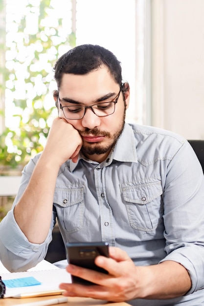 Bored executive using smart phone while working at the office desk