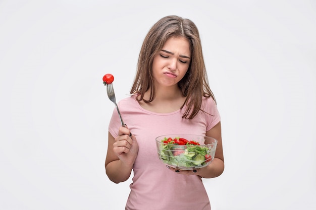 Bored jonge vrouw kijkt naar glazen kom met salade