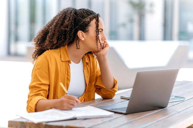 bored overworked brazilian or latino curly haired young woman freelancer female student sitting outdoors near campus with laptop looks sadly to the side feels exhausted bored thoughtful