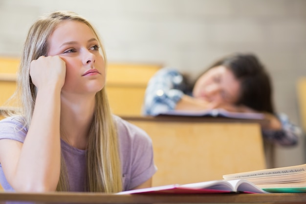 Foto bored student die terwijl klasgenoot die op universiteit slaapt luistert