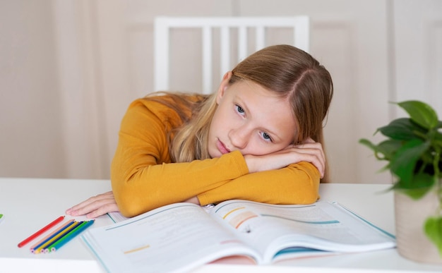 Bored teen girl sitting at table with book feeling tired