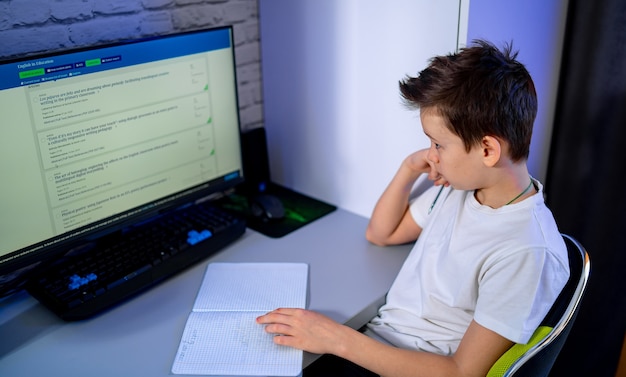 Bored teenage boy studing at computer. Doing tests. Tired and bored. Study in quarantine. Schoolboy during qurantine