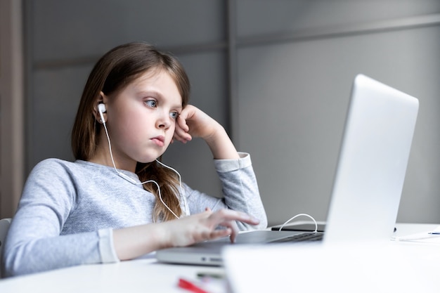 Bored teenage girl tired of online computer classes child looks at the monitor with sadness at home