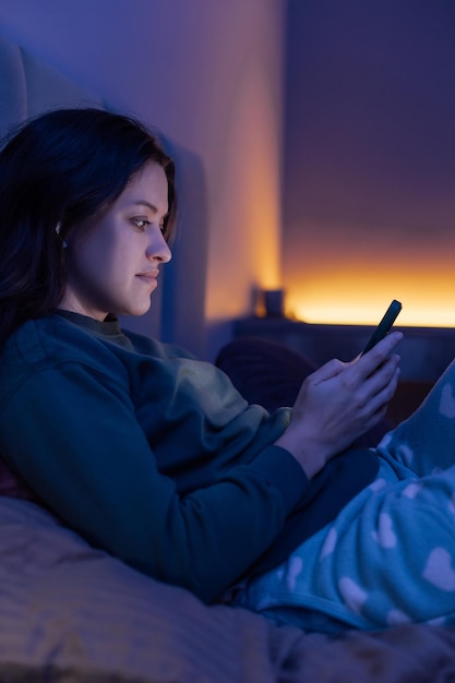 bored woman chatting and surfing on internet with smartphone late at night lying on bed