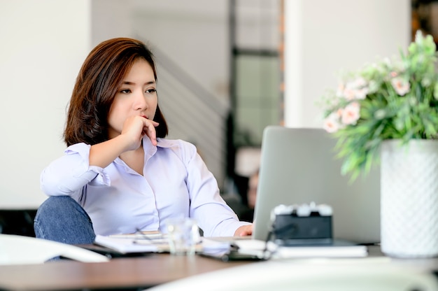 Bored young businesswoman sitting at office desk while working with laptop.