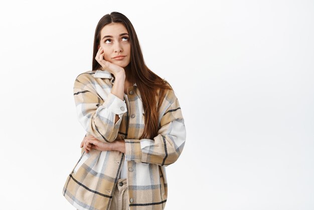 Bored young woman lean on hand and looking up daydreaming thinking or imaging something while sitting at boring meeting standing over white background