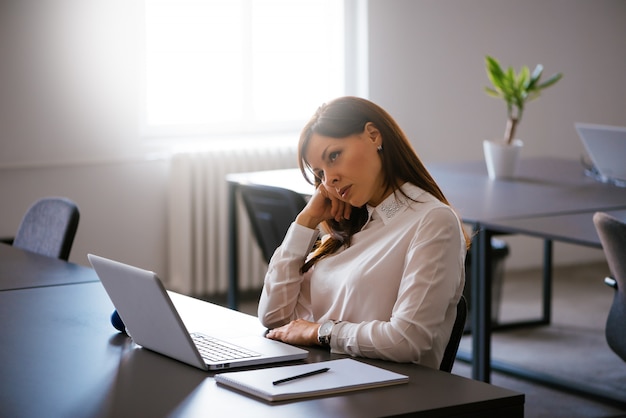 Giovane donna annoiata nell'ufficio che funziona con un computer portatile