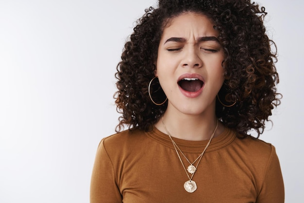 Boring. Bored uninterested sleepy attractive modern 20s curly-haired mixed race female yawning open mouth wide close eyes frowning falling asleep