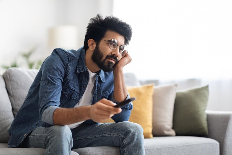 Photo boring show portrait of upset young indian guy watching tv at home