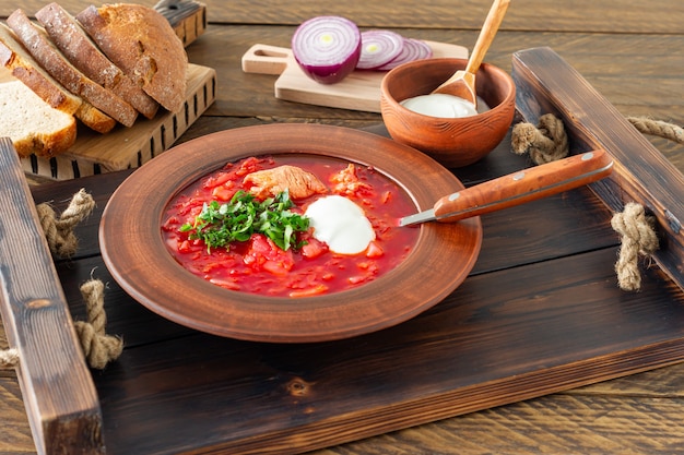 Borsch - traditionele Oekraïense en Russische bietensoep op donkere houten achtergrond. Geserveerd met roggebrood, knoflook en zout op houten dienblad.