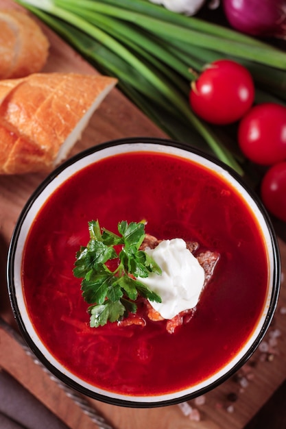 Borscht soup a on the dark rustic wooden table, with white slices bread and sour cream , green onion, view from above