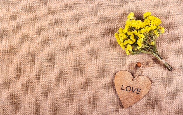 bos gele bloemen en houten hart op natuurlijke linnen achtergrond. Romantisch concept.