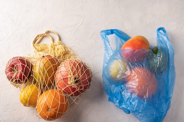 Bos van gemengde biologische groenten, fruit en groenten in een koordzak en plastic op lichte achtergrond.