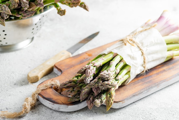 Bos van rauwe biologische asperges aan boord en in een vergiet klaar voor het koken van gezonde voeding op lichtgrijs marmer.