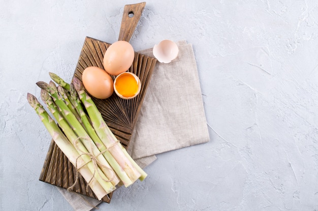 Bos van rauwe verse asperges met eieren op een grijze betonnen achtergrond