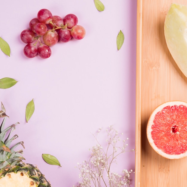 Bos van rode druiven; ananas; grapefruit en muskmelon met gypsophila bloem op roze achtergrond