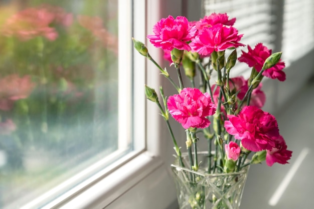 Bos van roze anjerbloemen in vaas op vensterbank die op vensterglas nadenken