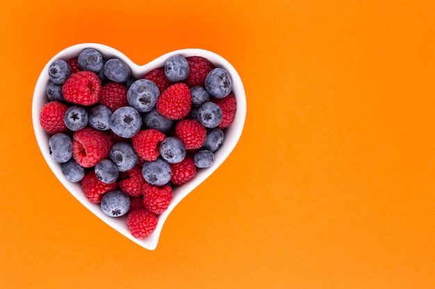 Bosbes en frambozen, fruit in een hartvormige schaal op een porseleinen kom