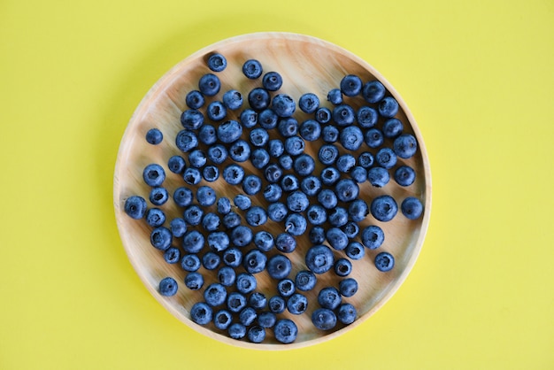 Bosbessenfruit in houten plaat op gele achtergrond.