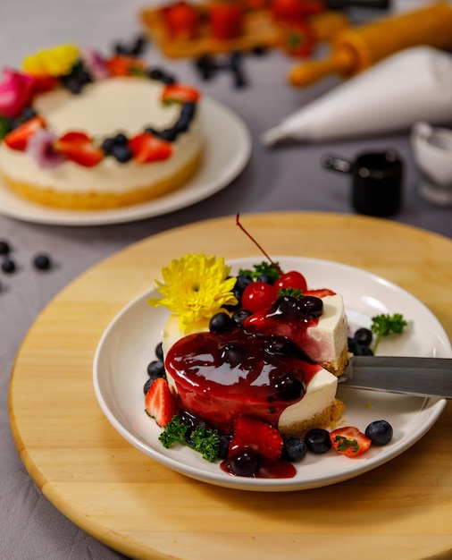 Bosbessensaus gieten op heerlijke zoete cheesecake versierd met verse bessen en bloemen op een houten bord, voor een verjaardag, Valentijnsdag en feest