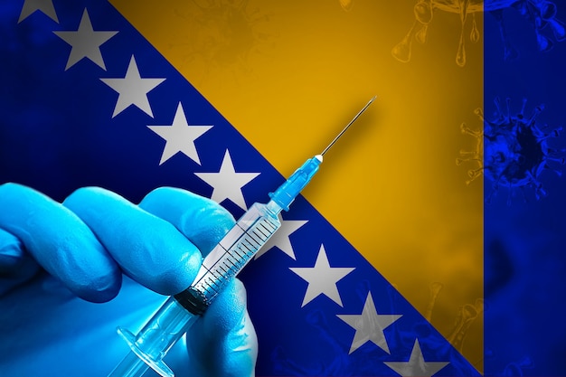 Bosnië en Herzegovina Covid19 vaccinatie Hand in een blauwe rubberen handschoen houdt spuit in vlag