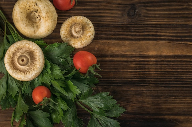 Foto bospaddestoelen twee tomaten en groenen op een houten ondergrond plat leggen