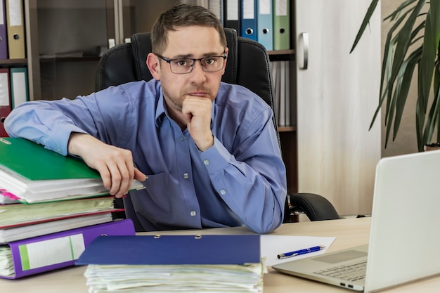 Boss businessman at his desk in the office with a bunch of folders with papers