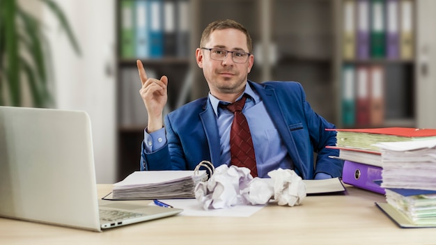 Boss businessman at his desk in the office with a pile of folders and crumpled paper