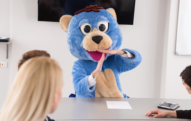 Boss dresed as teddy bear having fun with bussines people in\
modern corporate office