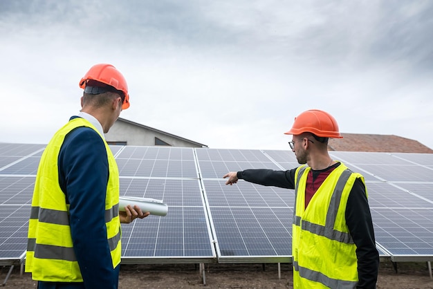 The boss in a helmet and vest stands with an employee in special clothes near the solar panels Green electricity concept