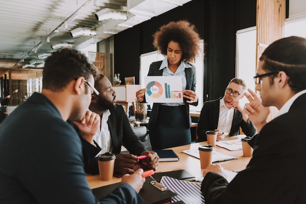 Photo boss is showing diagram to employees who sitting at table