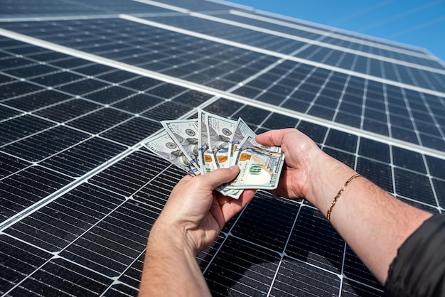 Boss in a jacket with young hands holding a large amount of dollars against the background of solar panels concept of green electricity