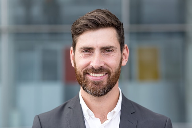 Photo boss man looking at camera and smiling, young businessman banker with beard photo with close up portrait