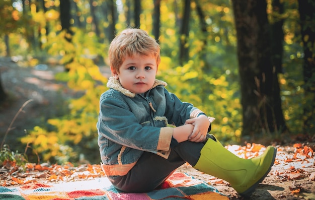 Bosschool is buitenonderwijs bezoek natuurlijke ruimtes jongen in rubberen laarzen ontspannen in het bos leuk toeristisch concept hij houdt van wandelen kind zit op geruite bospicknick kind ontspant in herfstbos