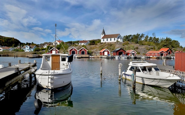 Boten afgemeerd in de haven van een klein zweeds vissersdorpje molle aan de kust met traditionele rode hutten en kerk op de heuvel