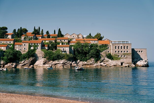 Boten liggen aangemeerd aan de rotsachtige kust van het eiland Sveti Stefan in Montenegro.