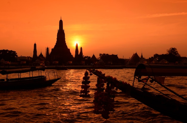 Boten zeilen in de rivier bij de tempel tegen de oranje hemel.