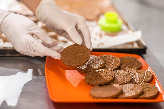 Boterkoekjes. Dient witte handschoenen in die klaar om rond chocoladekoekje over plaat te eten tonen, is het gezicht niet zichtbaar