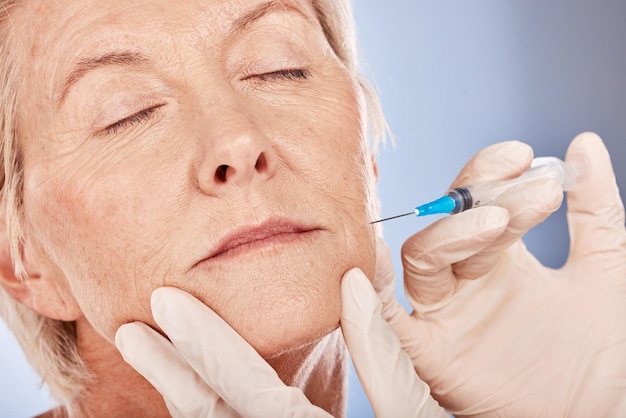 Botox-cosmetica en oudere vrouw met een schoonheidsspecialiste die een anti-verouderingsbehandeling doet in een studio Schoonheidshuidverzorging en oudere dame die cosmetische vulmiddelinjectie doet voor rimpels in het gezicht door grijze achtergrond