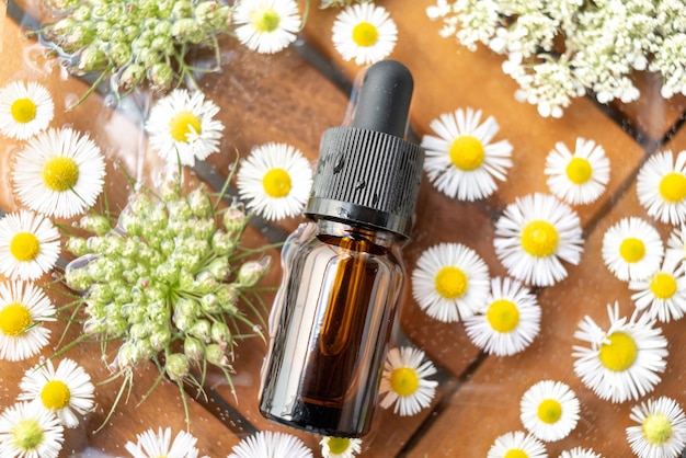 Bottle or battle for essential oil with a pipette lies in the water surrounded by flowers