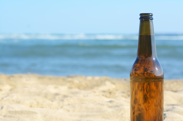 Bottle of beer on beach near sea closeup Space for text