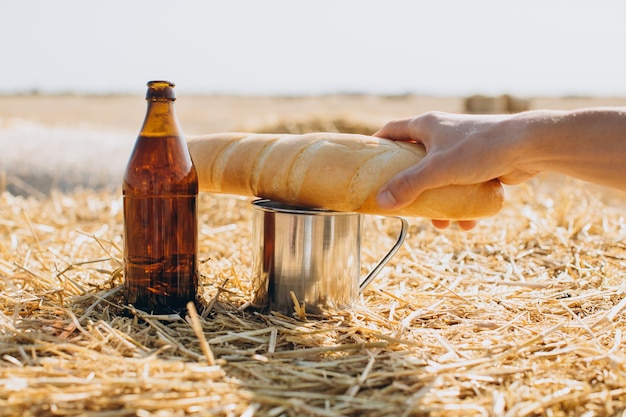 Bottle of beer bread and metal mug on wheat field background