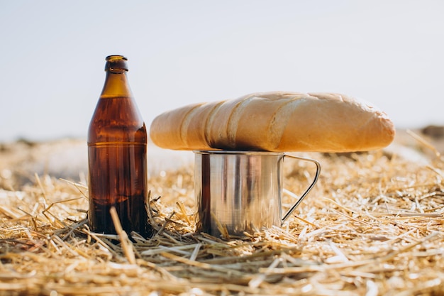 Bottle of beer bread and metal mug on wheat field background